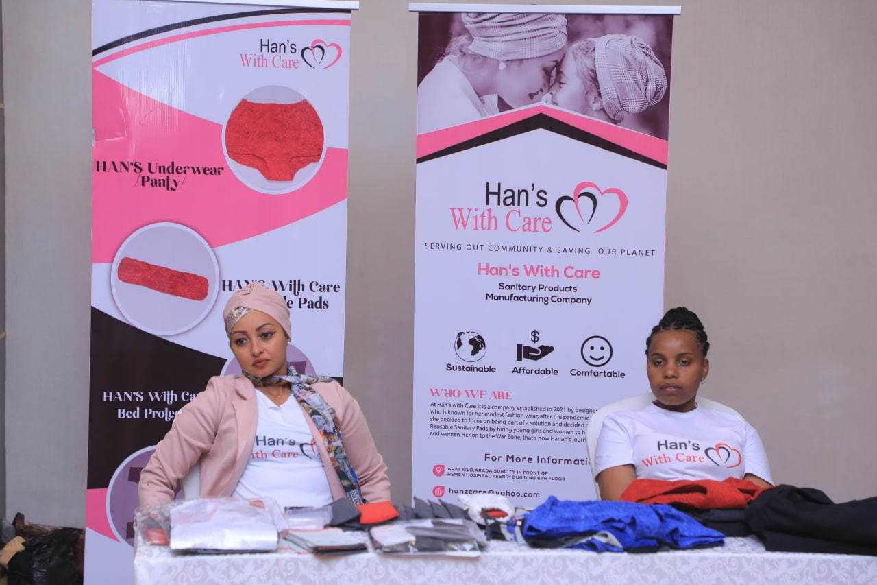 Exhibitors and packaged menstrual products beside Han’s With Care banners showing underwear and reusable pads.