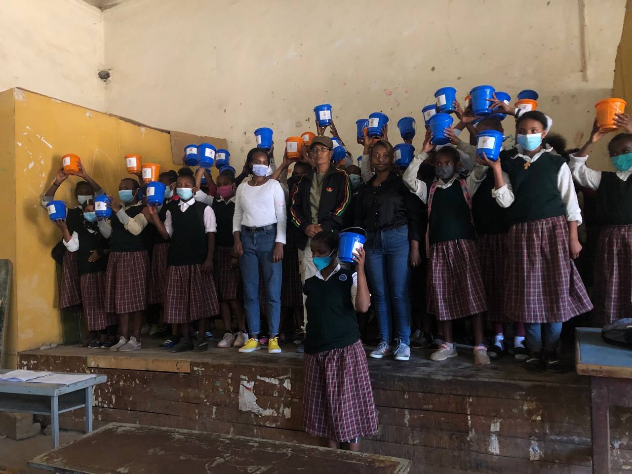 Participants holding blue and orange dignity buckets at a school gathering.
