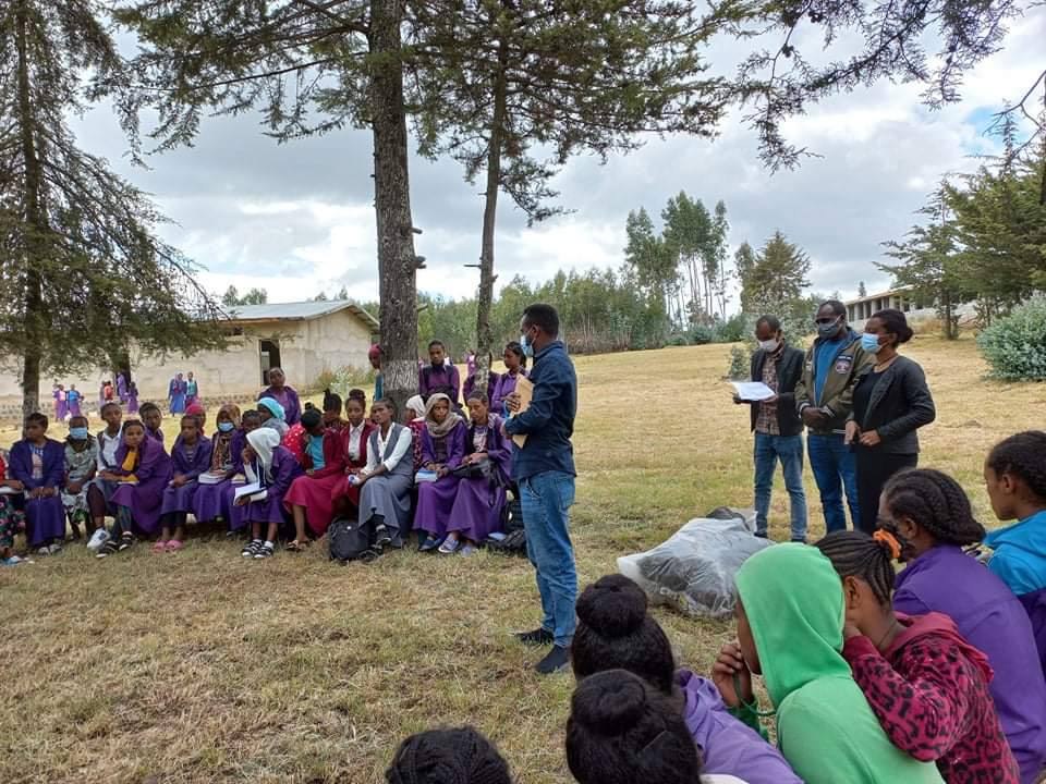 A group listening to speakers outdoors under trees.