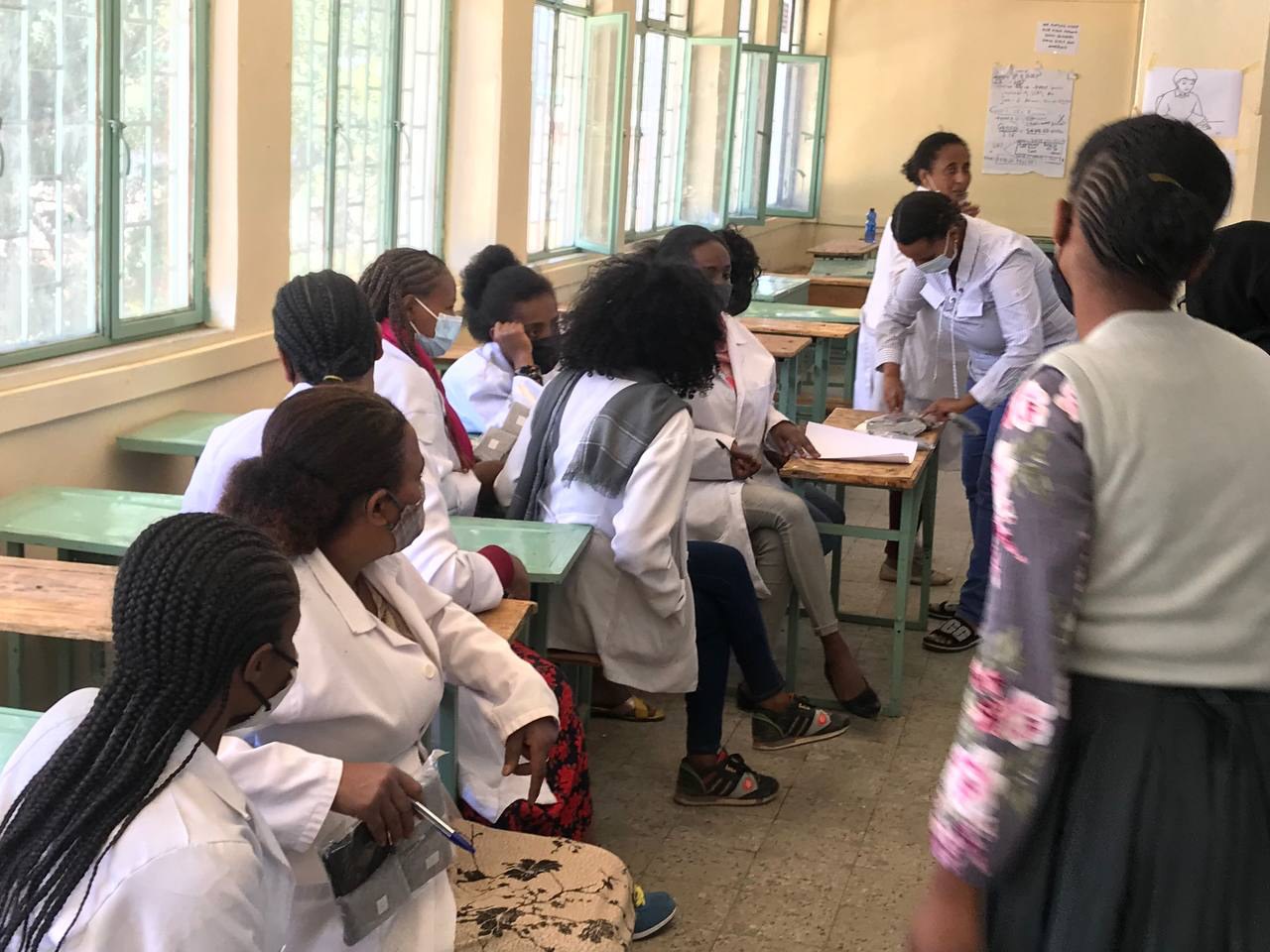 Participants gathered around a classroom desk while a facilitator demonstrates materials.