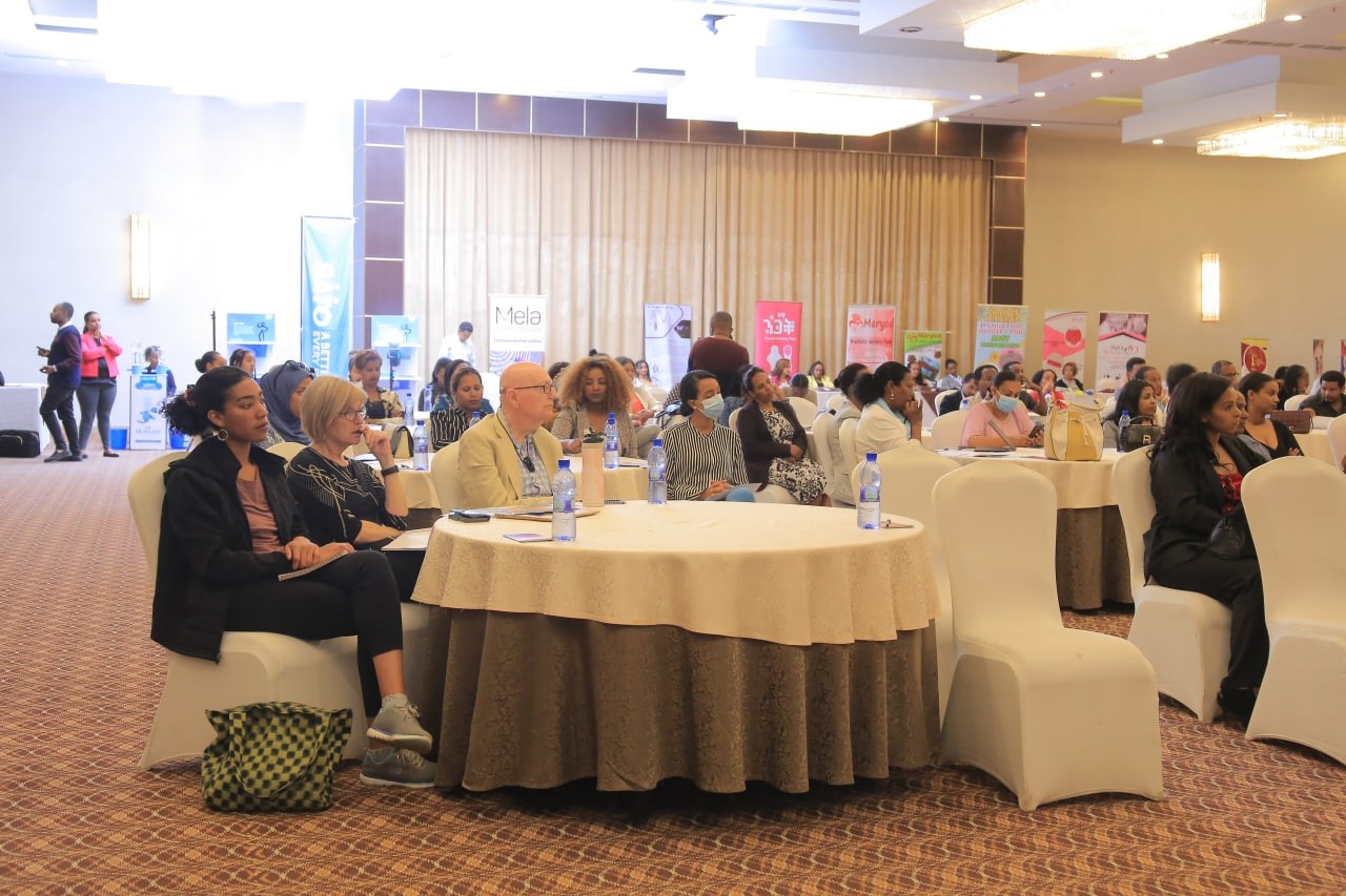 Participants seated at round tables during a dialogue with exhibition banners in the room.